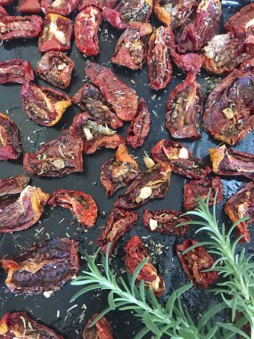 Bir fırın tepsisine baharat ve sarımsak ile güneşte kurutulmuş domates. Onların üzerinde taze biberiye yatıyor.