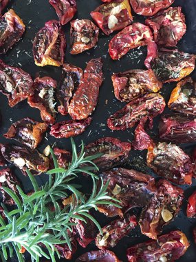 Bir fırın tepsisine baharat ve sarımsak ile güneşte kurutulmuş domates. Onların üzerinde taze biberiye yatıyor.