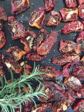 Bir fırın tepsisine baharat ve sarımsak ile güneşte kurutulmuş domates. Onların üzerinde taze biberiye yatıyor.