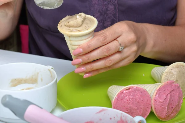 Helado casero de fresa y plátano. En cuernos comestibles en un plato. Una mujer llena el cuerno con helado . — Foto de Stock