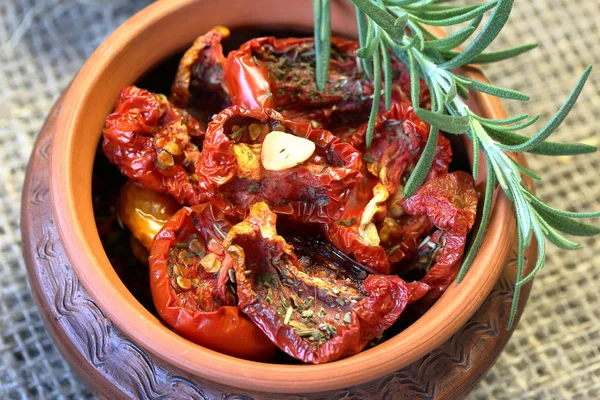 Sun-dried tomatoes with spices and garlic in a clay pot. On it is a branch of rosemary. — Stock Photo, Image