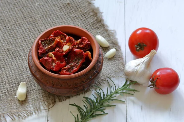 Tomates secados pelo sol com temperos e alho em um pote de barro. Perto de alecrim, tomates e alho . — Fotografia de Stock