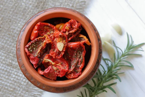 Sun-dried tomatoes with spices and garlic in a clay pot. Near rosemary and garlic. — Stock Photo, Image