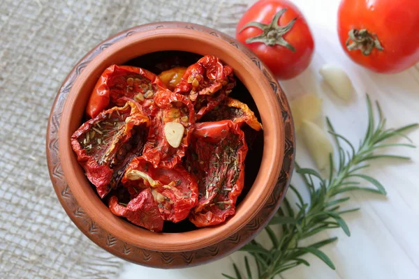 Sun-dried tomatoes with spices and garlic in a clay pot. Near rosemary, tomatoes and garlic. — Stock Photo, Image