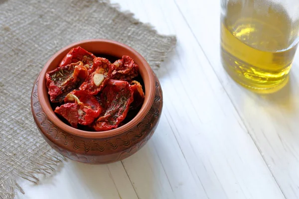 Sun-dried tomatoes with spices and garlic in a clay pot. Nearby is a bottle of olive oil. — Stock Photo, Image
