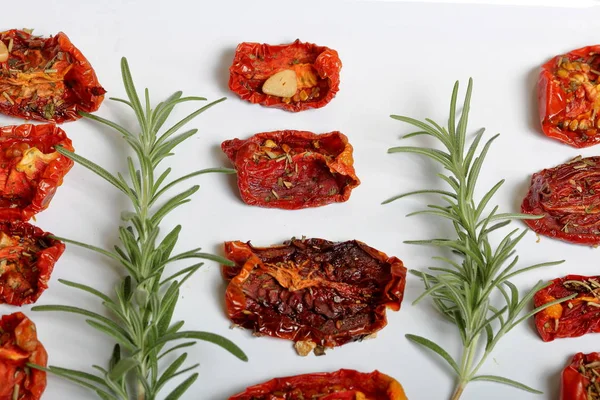 Sun-dried tomatoes with spices and garlic on a light tray. Nearby lies fresh rosemary. — Stock Photo, Image