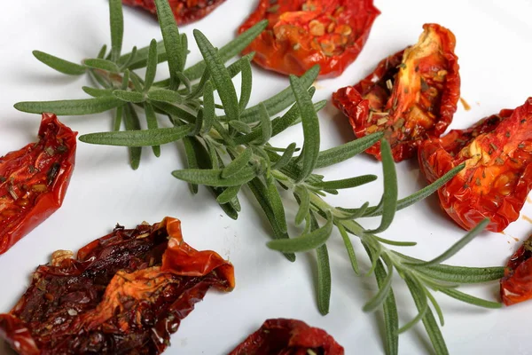 Sun-dried tomatoes with spices and garlic on a light tray. Nearby lies fresh rosemary. — Stock Photo, Image