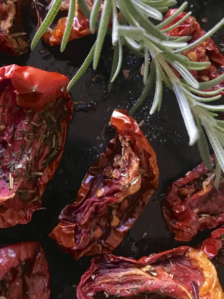 Sun-dried tomatoes with spices and garlic on a baking sheet. On top of them lies fresh rosemary. Close up. — Stock Photo, Image