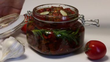 Kadın bir kavanoz kurutulmuş domates kapatır. Bir kavanozda domates ile biberiye, sarımsak ve baharat bir dal. Zeytinyağı ile dökülür