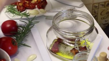 Bir kadın zeytinyağı, tuz ve baharat ile bir kavanoza kurutulmuş domates koyar.