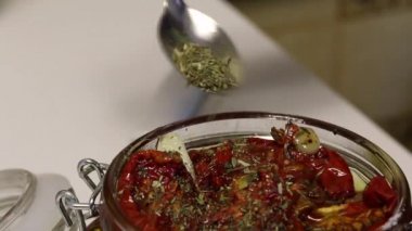 Bir kadın kurutulmuş domates kavanozuna baharat ekler. Biberiye, sarımsak ve baharat dalvardır. Zeytinyağı ile dökülür..