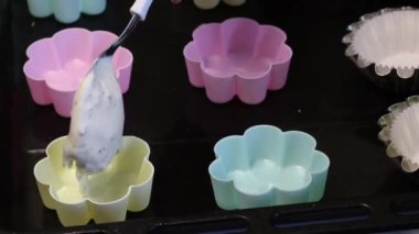 Bir kadın hamuru silikon kek pişirme tabaklarına koyar. Farklı renklerde şekiller. Tatlı pişirmek..