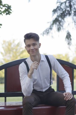 Şık giyimli genç adam bir park bankında oturur. Bir gülümseme ile kameraya bakmak.