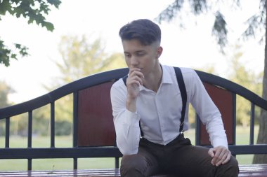 Şık giyimli genç adam bir park bankında oturur. Başka bir yere bakıyor ve gülüyor..