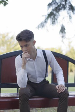 Şık giyimli genç adam bir park bankında oturur. Başka bir yere bakıyor ve gülüyor..