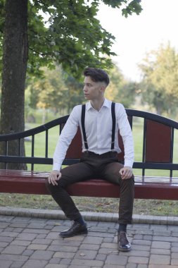 Şık giyimli genç adam bir park bankında oturur. Başka bir yere bakıyor ve gülüyor..