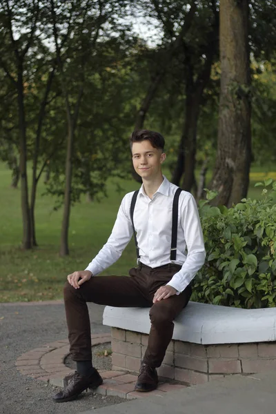 Jeune homme élégamment habillé posant dans un parc. Assis sur le trottoir et regarde la caméra . — Photo