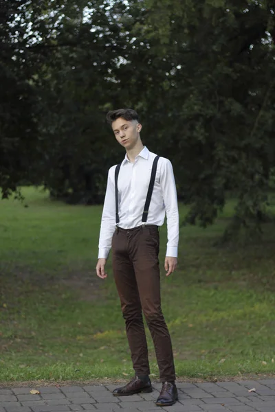 Şık giyimli genç adam bir parkta poz. Küstahçe kameraya bakıyor.