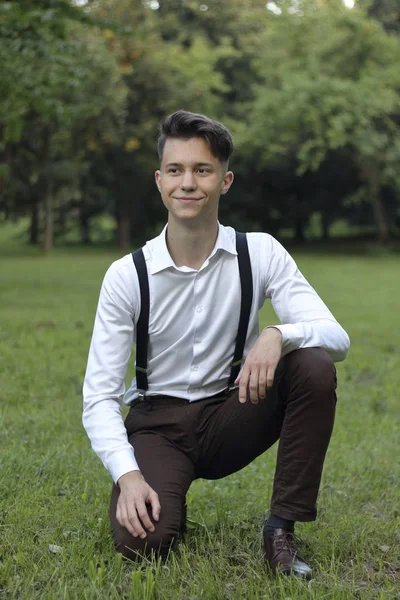 Jovem elegantemente vestido posando em um parque. Senta-se no gramado e olha para o lado . — Fotografia de Stock