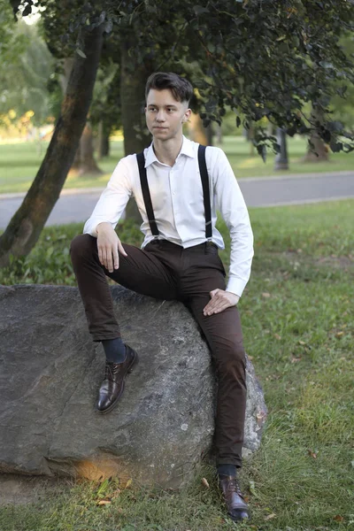 Jovem elegantemente vestido senta-se em uma pedra de pedra no parque. Com um olhar atencioso . — Fotografia de Stock