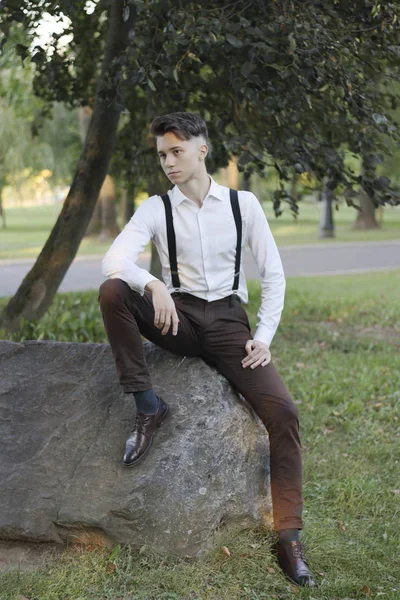 Élégamment habillé jeune homme assis sur un rocher de pierre dans le parc. Avec un regard réfléchi . — Photo