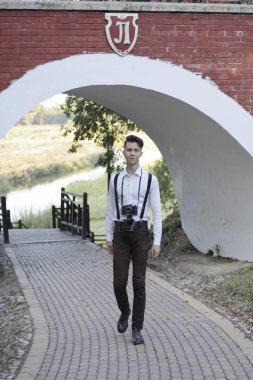 Şık giyimli genç adam parkta yürüyor. Elinde bir Slr film kamera tutar.