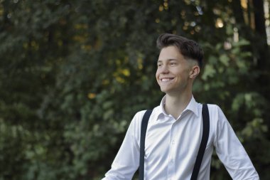 Şık giyimli genç adam bir parkta poz. Gülmek uzaklara bakıyor.