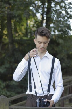Şık giyimli genç adam bir parkta poz. Elinde bir Slr film kamera tutar.