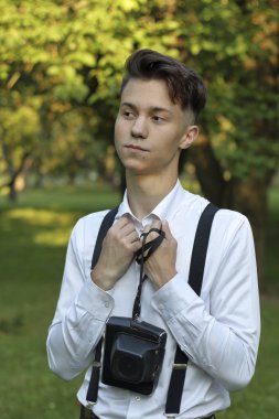 Şık giyimli genç adam bir parkta poz. Gülmek ellerini göğsüne getirir. Bir durumda kameranın elinde.