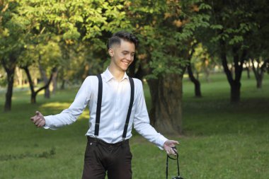 Şık giyimli genç adam bir parkta poz. Gülmek çaresiz bir jest yapar.