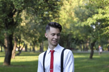 Şık giyimli genç adam bir parkta poz. Bir Slr film kamera omzuna asılı.