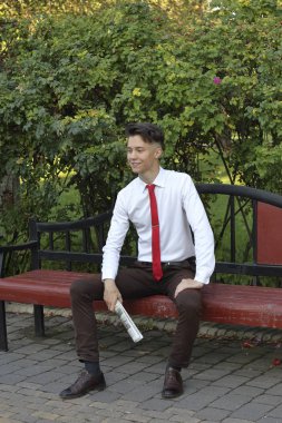 Şık giyimli genç bir adam bir park bankında oturur ve elinde bir gazete tutar. bir gülümseme ile uzağa bakar.