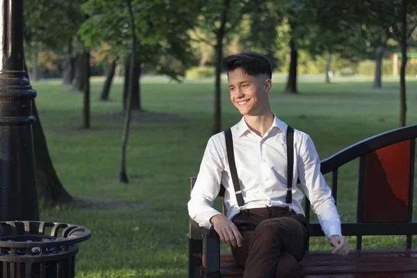 Stijlvol gekleed jonge man zit op een park bank. Hij kijkt weg en lacht. — Stockfoto