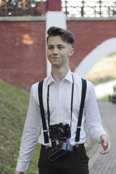 Şık giyimli genç adam parkta yürüyor. Elinde bir Slr film kamera tutar. — Stok fotoğraf