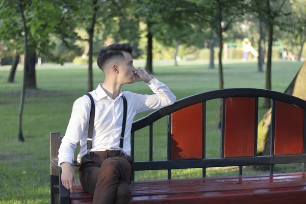 Jovem elegantemente vestido senta-se em um banco de parque e olha atenciosamente para o lado . — Fotografia de Stock