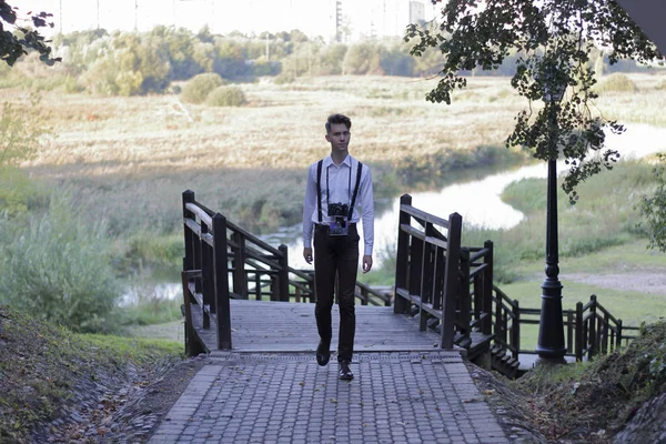 Un jeune homme élégamment habillé se promène dans le parc. Dans ses mains tient un appareil photo reflex . — Photo