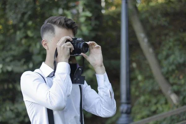 Elegantemente vestido joven se sienta a tomar fotos en el parque. En sus manos sostiene una cámara de película SLR . — Foto de Stock