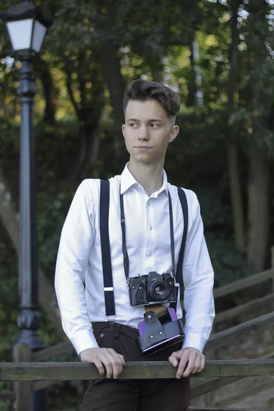 Şık giyimli genç adam bir parkta poz. Bir Slr film kamera boyun asılı. — Stok fotoğraf