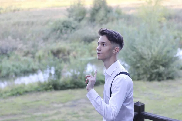 Stylishly dressed young man posing in a park. Raising a finger to the top, he listens warily. — Stock Photo, Image