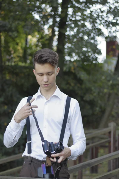 Jeune homme élégamment habillé posant dans un parc. Dans ses mains tient un appareil photo reflex . — Photo