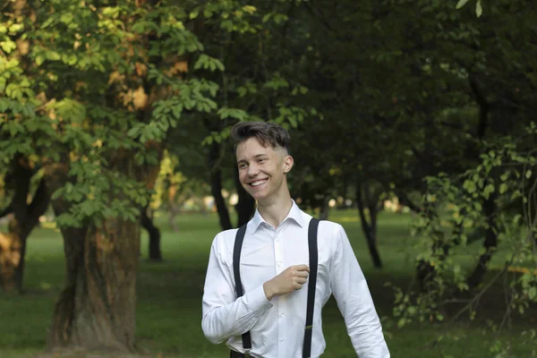 Stijlvol gekleed jonge man poseren in een park. Lachen, naar de zijkant kijken, zijn hulp aanpassen. — Stockfoto