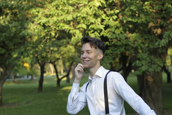 Jeune homme élégamment habillé posant dans un parc. Riant, regarde sur le côté, touche le menton . — Photo