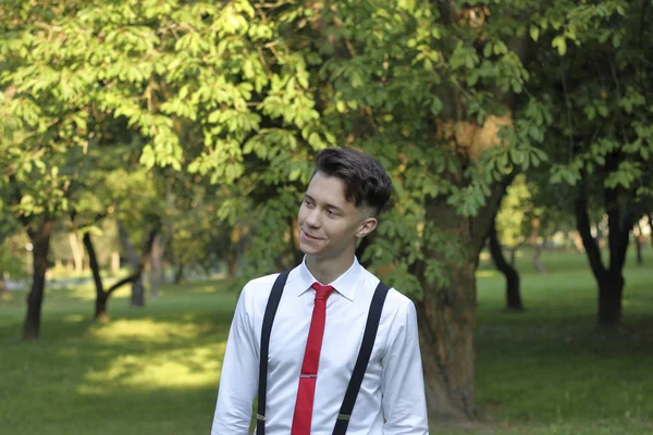 Jovem elegantemente vestido posando em um parque. Uma câmera de filme SLR pendura em seu ombro . — Fotografia de Stock