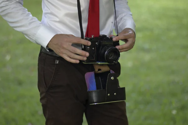 Şık giyimli genç adam bir parkta poz. Bir Slr film kamera boyun asılı. — Stok fotoğraf