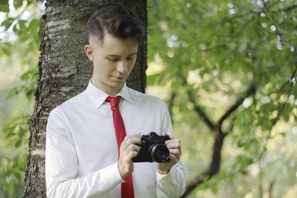 Jeune homme élégamment habillé posant dans un parc. Tient la caméra dans ses mains et fonctionne avec les paramètres . — Photo