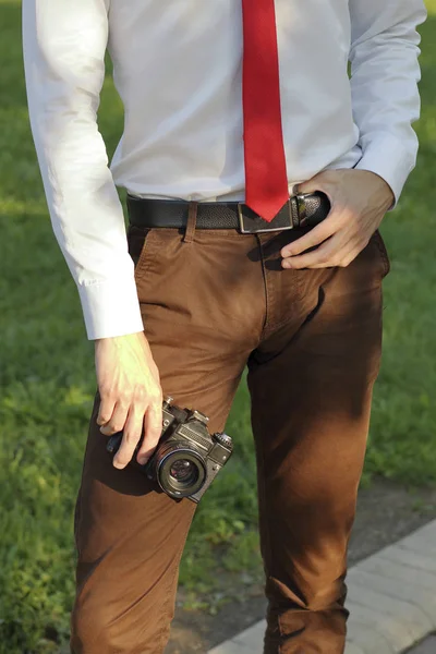 Jeune homme élégamment habillé posant dans un parc. Dans ses mains tient un appareil photo reflex . — Photo