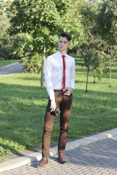 Jeune homme élégamment habillé posant dans un parc. Dans ses mains tient un appareil photo reflex . — Photo