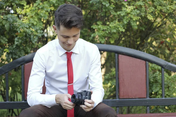 Şık giyimli genç bir adam bir park bankında oturur. Şık giyimli genç adam bir park bankında oturur. Elinde bir Slr film kamera tutar. — Stok fotoğraf