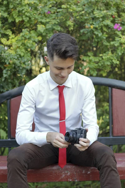 Şık giyimli genç bir adam bir park bankında oturur. Şık giyimli genç adam bir park bankında oturur. Elinde bir Slr film kamera tutar. — Stok fotoğraf