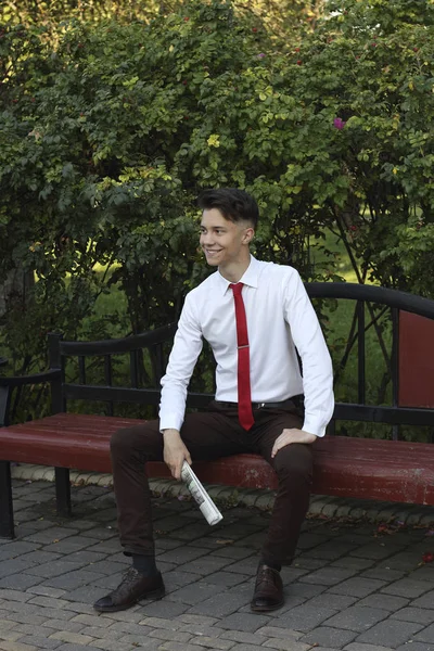 Стильно одягнений молодий чоловік сидить на лавці парку і тримає в руках газету. озирається з посмішкою . — стокове фото